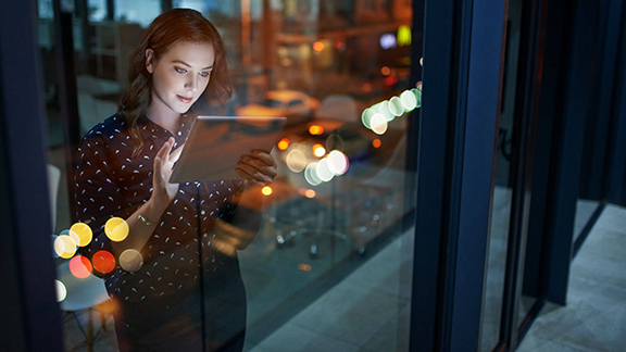 A woman working on a tablet while standing against a window