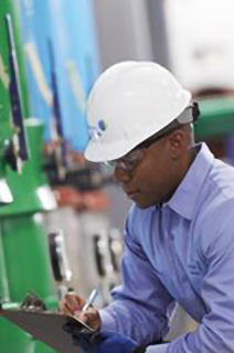 An engineer in safety helmet taking down notes while inspecting an hvac equipment
