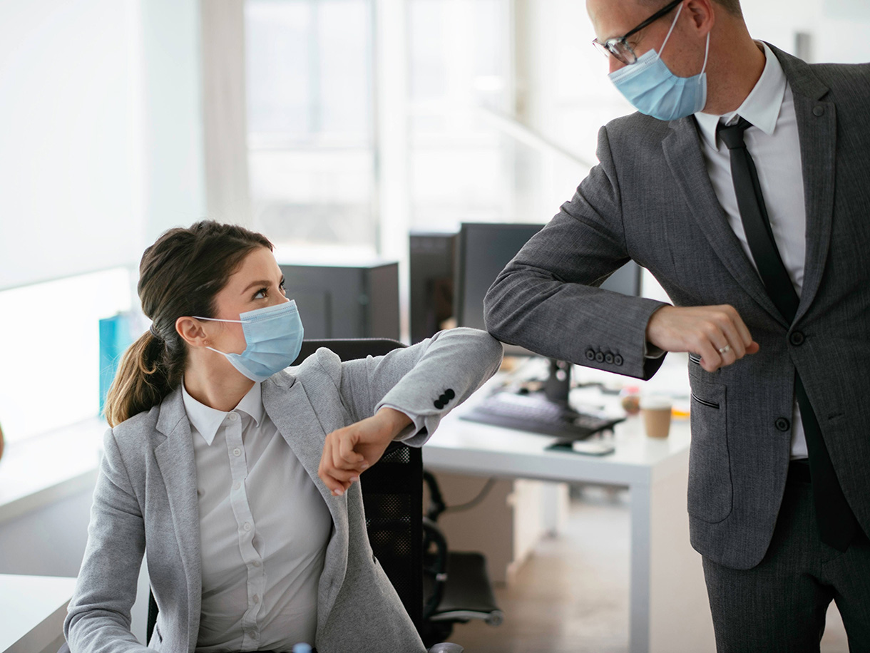 A man and a woman bumping elbows while wearing masks in an office