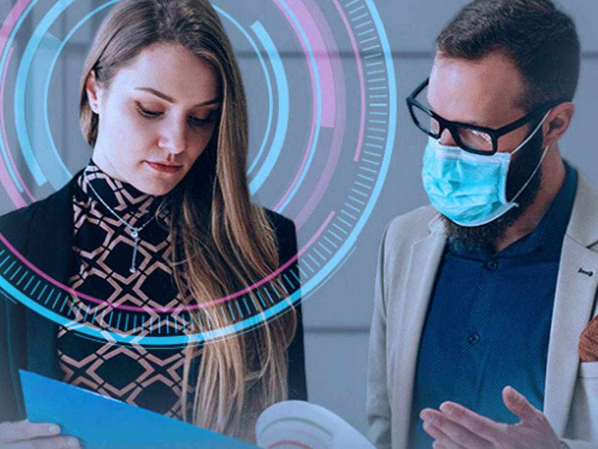 A man wearing a mask discussing work with a woman in an office