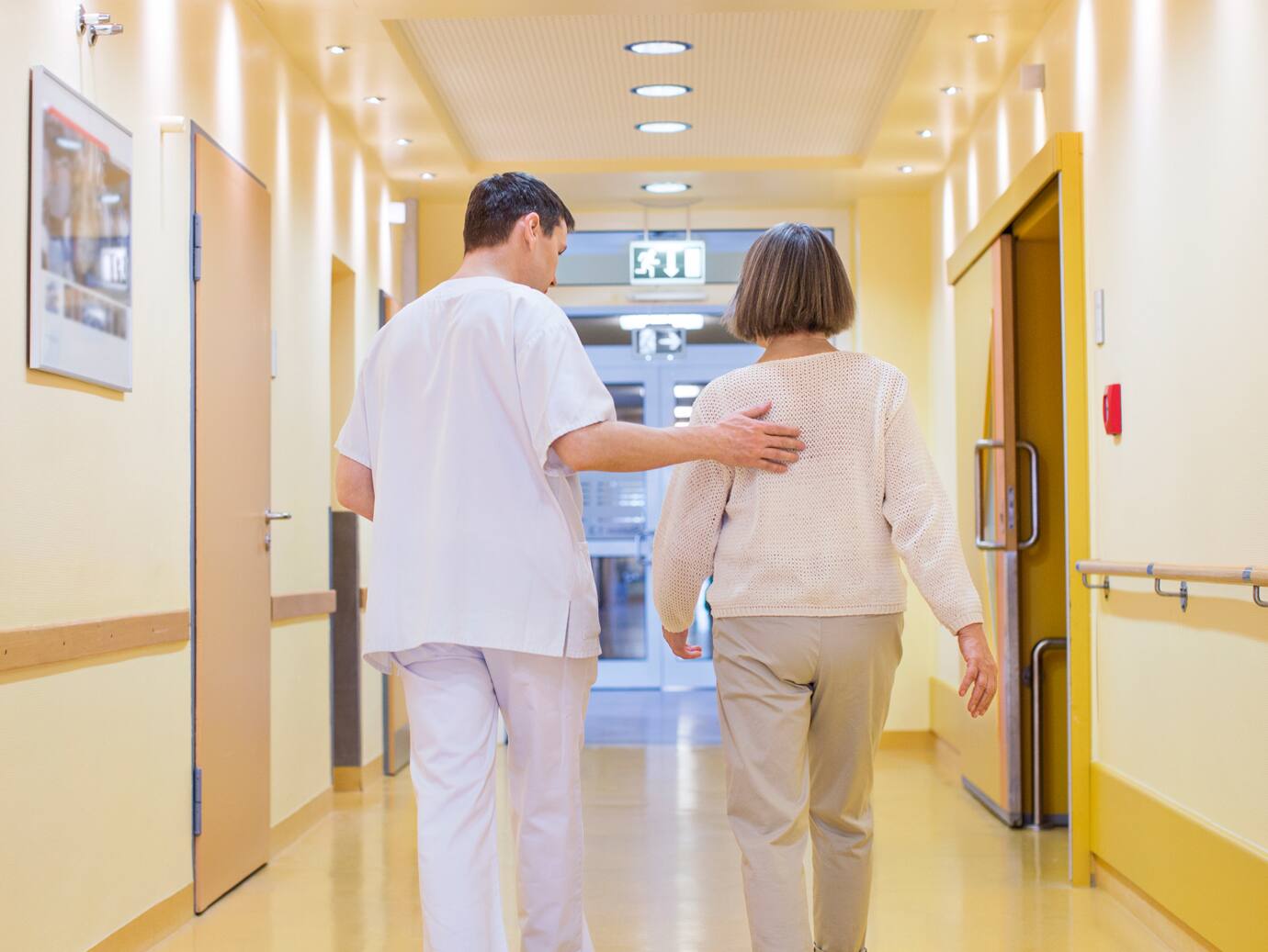 A doctoring escorting a patient down the hallway with his hands on her back